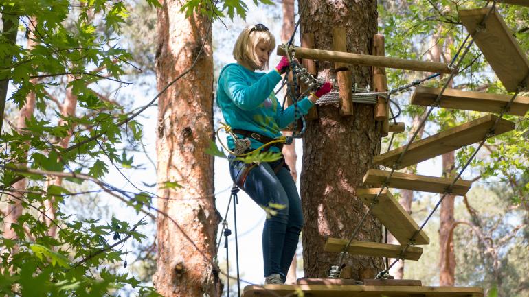 一位女性正准备穿过 Go Ape Treetop Adventure 冒险乐园绳索项目场地中的曲桥