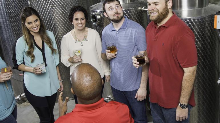 一群人在 Donner-Peltier Distillers 酿酒厂一边观看酿酒工艺，一边品尝美酒