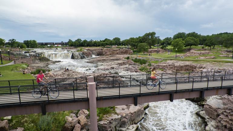 在南达科他州苏福尔斯的瀑布公园内骑车穿过横亘在瀑布上方的桥梁