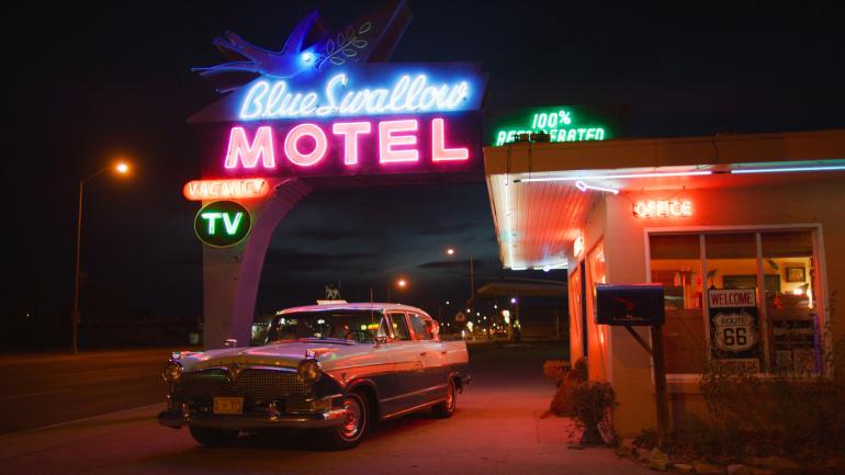 新墨西哥州图克姆卡里的 Blue Swallow Motel 汽车旅馆外有一辆老式汽车和标示旅馆名称的霓虹灯