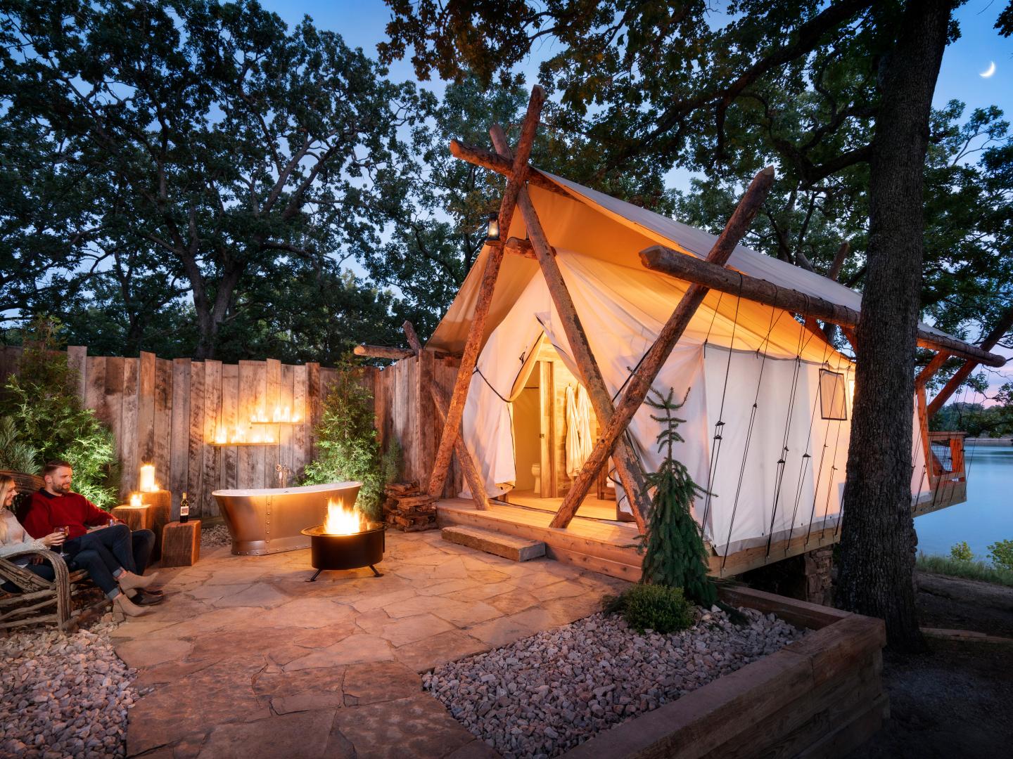 在密苏里州里奇代尔 Big Cedar Lodge 旅馆的长溪营地，一对情侣在篝火和露营帐篷旁放松身心