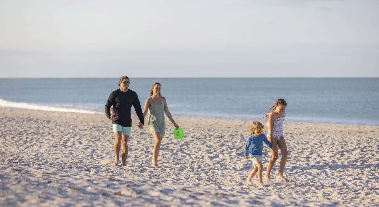 一家人沿着佛罗里达州夏洛特县唐佩德罗岛 (Don Pedro Island) 的白沙海岸悠闲漫步
